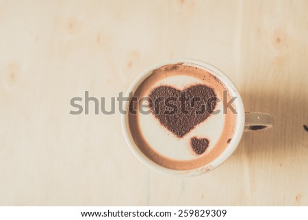 Heart shape on coffee cup on wooden background with vintage colour effect. Still life.