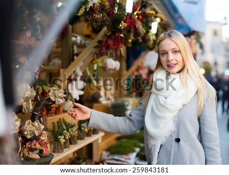 Pretty young woman with long blond hair choosing floral compositions at a christmas market