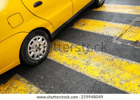 Yellow taxi car stands on pedestrian crossing with lines as a road marking
