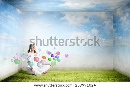 Young smiling girl sitting on grass and meditating
