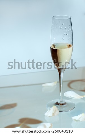 Glass of champagne on the table, strewn with rose petals
