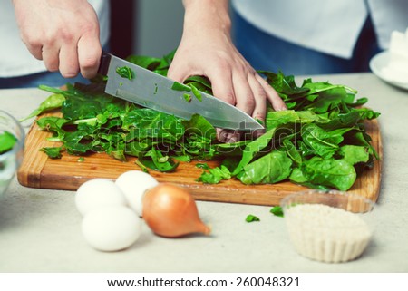 Vegetarian bakery concept. Chef's hands cutting spinach salad in kitchen of cafe, restaurant. Close up. Indoor shot Royalty-Free Stock Photo #260048321