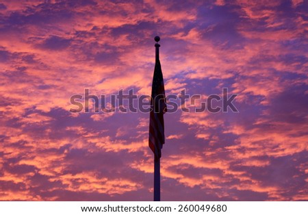 A Silhouetted American Flag Against a Beautiful Dramatic Cloudscape with Bright Pink, Red, and Blue Clouds Basking in the Light of the Rising Sun