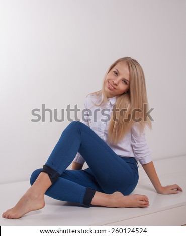 Blonde young woman in ragged jeans and vest sitting on floor on  white background