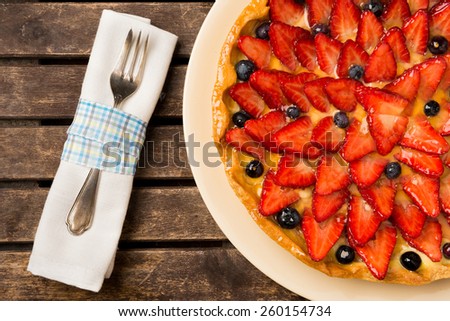 Strawberry and blueberry cake on wooden background. Composition with a napkin and a vintage fork