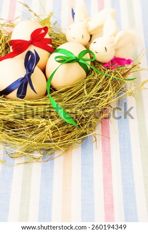 Easter eggs and two rabbits in nest on stripe textile background