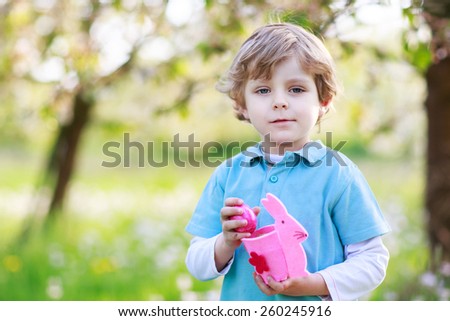 Adorable little boy celebrating Easter holiday and making egg hunt, having fun outdoors.