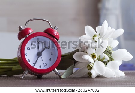 Red alarm clock and small bouquet of snowdrops.