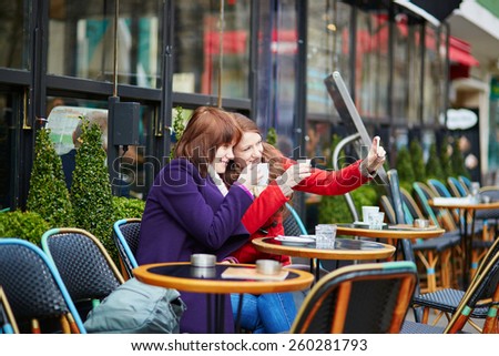 Two cheerful girls making self picture (selfie) in a Parisian street cafe
