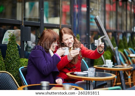 Two cheerful girls making self picture (selfie) in a Parisian street cafe