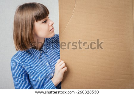 Banner sign woman peeking over edge of blank empty paper billboard with copy space for text. Beautiful Caucasian woman looking surprised and scared - funny. Isolated.