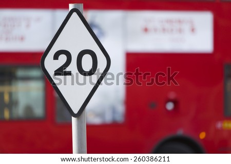 Speed limit sign of 20 in a city district with a red blurred bus in the background
