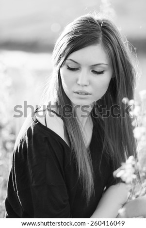 Beautiful girl with long, straight hair posing in the field looking melancholic. Black and white photography