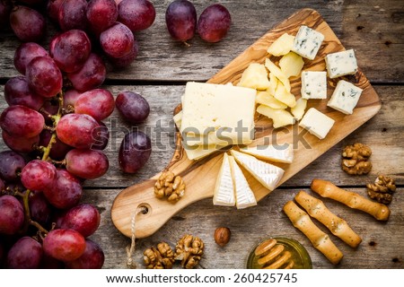 Cheese plate: Emmental, Camembert cheese, blue cheese, bread sticks, walnuts, hazelnuts, honey, grapes on wooden table Royalty-Free Stock Photo #260425745