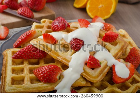 Homemade waffles with maple syrup and strawberries, topped fresh cream, orange fresh beverage