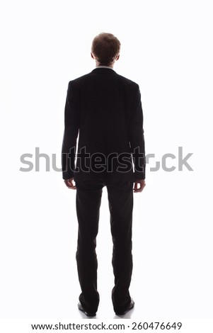Handsome man in a black suit and tie to his full height, he stands with his back to the camera on a light background                                