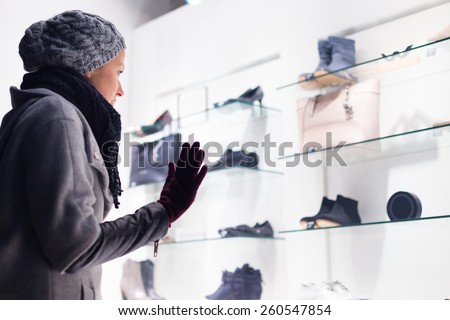Casualy winter dressed lady window shopping in front of sinfully expensive boutique store dispaly window. Customer woman in shopping street, looking at window, outdoor.