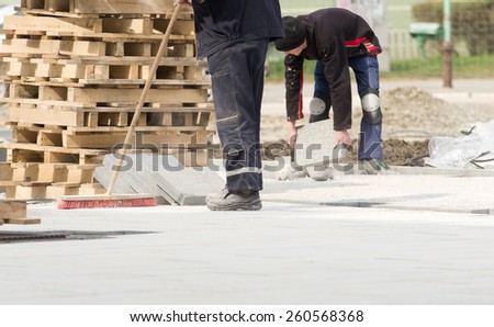 Construction worker in safety clothes cleaning building site after installing flagstones in sand