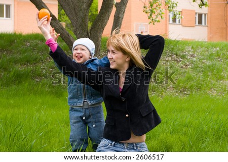 Mom and the son play with an orange on a grass. Spring.