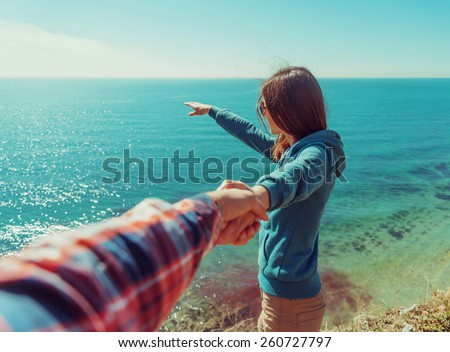 Couple in love. Beautiful young woman holding man's hand and showing him something in distance the sea. Point of view shot Royalty-Free Stock Photo #260727797