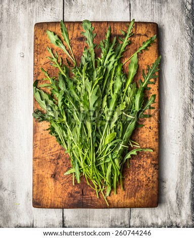 Fresh arugula on cutting board and white wooden table , top view