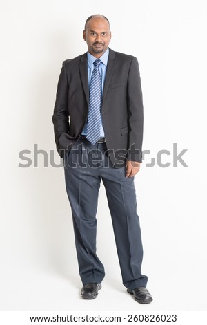 Full body Indian business man in formal suit looking at camera, standing on plain background.