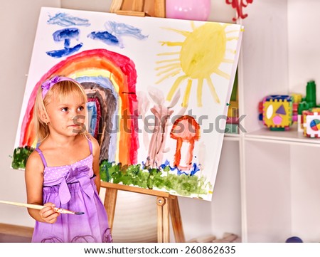 Little girl painting at easel in school. Education.