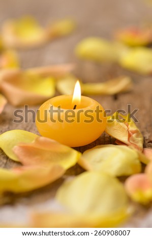 Orange roses petals with candle on old wooden board