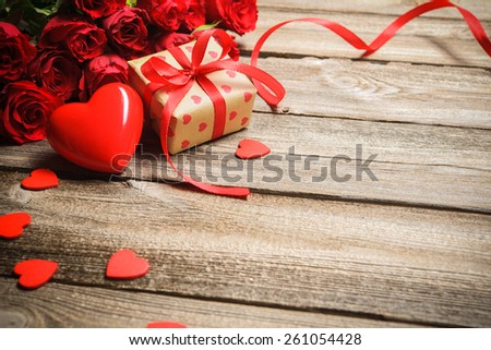 Bunch of roses with a gift box and red heart on wooden background