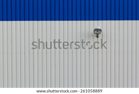 Lamppost on corrugated exterior wall. Abstract simmetry and minimal background.