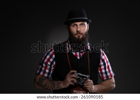 Bearded man in a hat holding an old camera - gray background