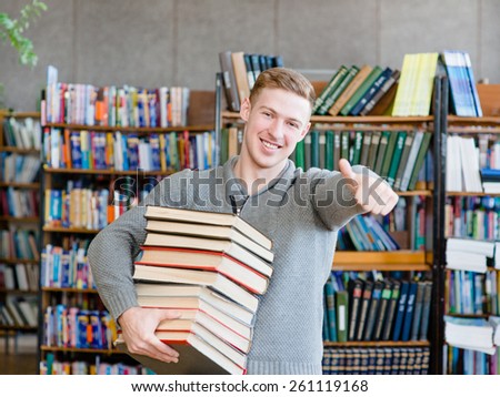 student with pile books showing thumbs up in college library