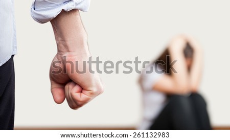 Family violence and aggression concept - furious angry man raised punishment fist over scared or terrified woman sitting at wall corner Royalty-Free Stock Photo #261132983