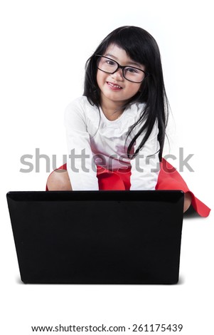 Cute little girl sitting in the studio and smiling at the camera while using laptop computer, isolated on white