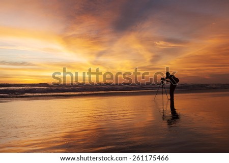 Male photographer taking picture with dslr camera on the beach at sunset time