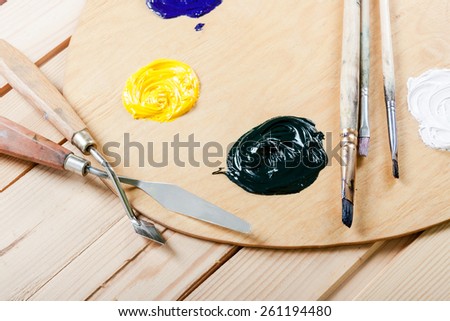 Palette with oil paint and brushes, on the wooden background.