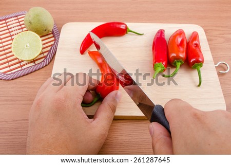  Man slicing Chilli pepper and lemons with Knife on chopping board on wooden background.