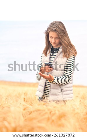 Beautiful young girl in field taking picture of wheat by smartphone. Fields of North Scotland. Outdoors.