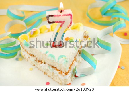 slice of seventh birthday cake with lit candle, confetti, and ribbon (shallow depth of field)