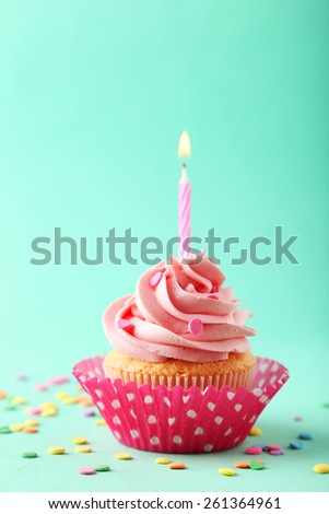 Tasty cupcake with candle on green background