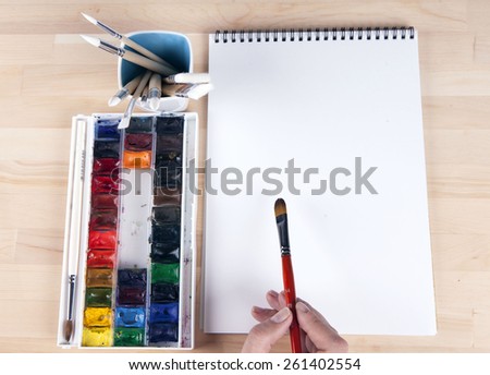 Beautiful composition of watercolor paints, brushes, album artist, with the artist's hand.