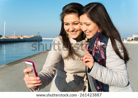 Two young smiling girls taking a selfie self portrait with mobile telephone at the beach. Enjoying the holidays, having fun and best friends concept