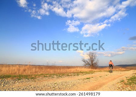 Wide open road and distant cyclist woman under blue sky and white clouds