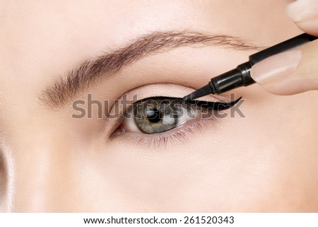 Beautiful model applying eyeliner closeup on eye Royalty-Free Stock Photo #261520343