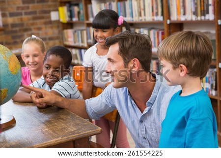 Cute pupils and teacher looking at globe in library at elementary school Royalty-Free Stock Photo #261554225