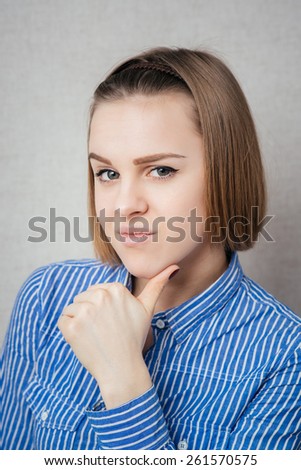 Young adult looking at you while holding chin gray background