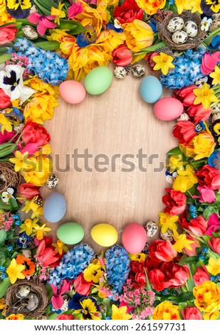 Easter decoration with spring flowers and colored eggs. Tulips, narcissus, hyacinth and pansy blossoms. Holidays background with space for your text