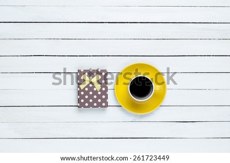Cup of coffee and gift on white wooden background