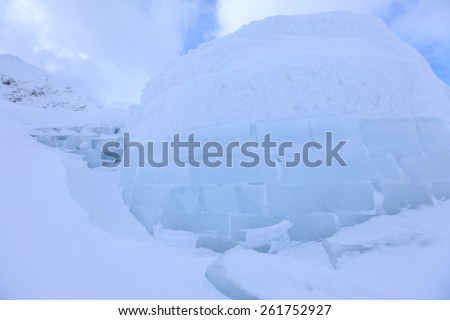 Igloo and snow shelter in high snowdrift with mountains peaks on background
