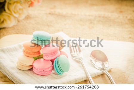 Macarons in a dish with flowers on wooden table in the vintage backgrounds,soft focus.